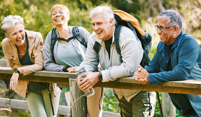four seniors laughing on a bridge while on a hike